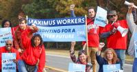 a group of workers wearing red t-shirts holding On Strike Against Maximus signs