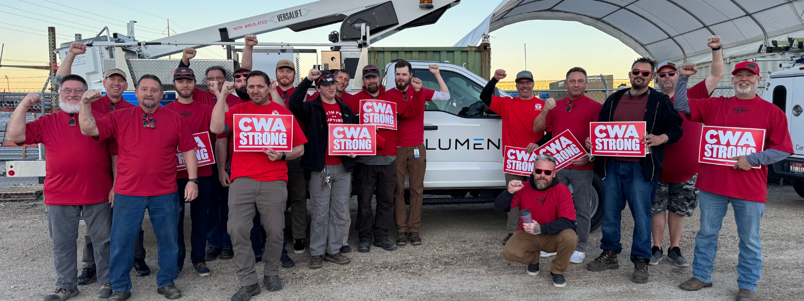 Lumen CWA workers stand in front of Lumen truck wearing red and holding their fists in the air.